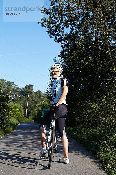 Reife Radlerin mit Fahrrad auf der Landstraße