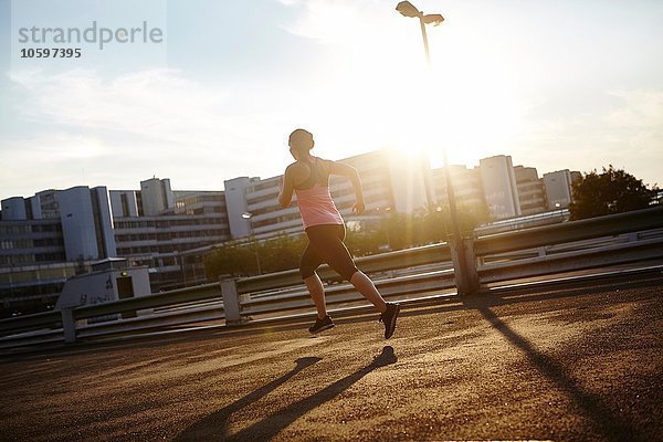 Sonnenstrahlende Silhouette einer jungen Läuferin auf dem Dach