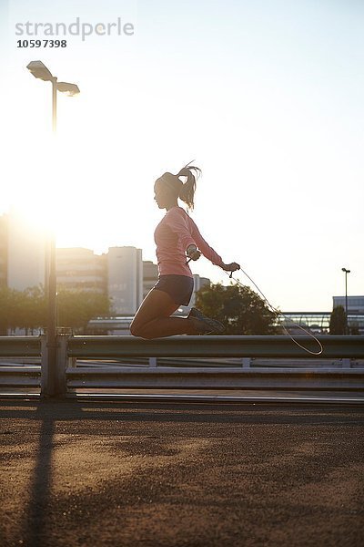 Sonnenstrahlende Silhouette einer jungen Frau beim Springen auf dem Dach