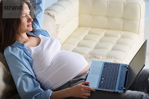 Schwangere Frau auf dem Sofa sitzend  mit Laptop