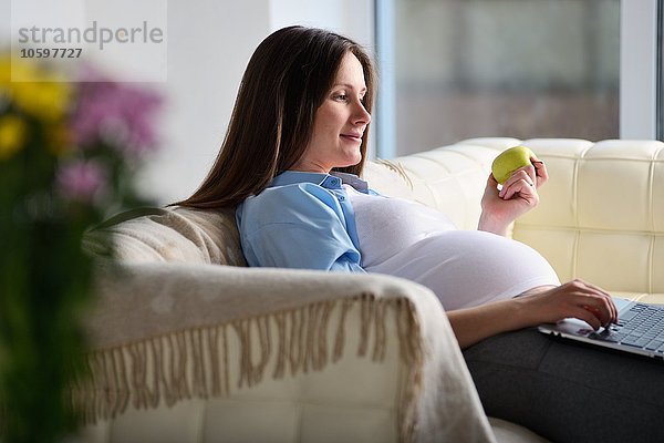 Schwangere Frau auf dem Sofa sitzend  mit Laptop