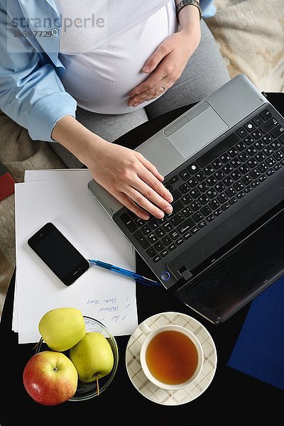 Schwangere Frau auf dem Sofa sitzend  mit Laptop  Ansicht über Kopf