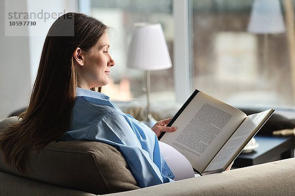 Schwangere sitzend auf dem Sofa  Lesebuch