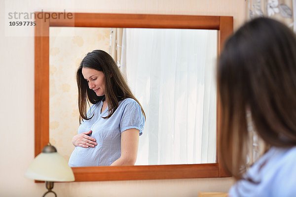 Schwangere Frau  die den Bauch hält  vor dem Spiegel stehend