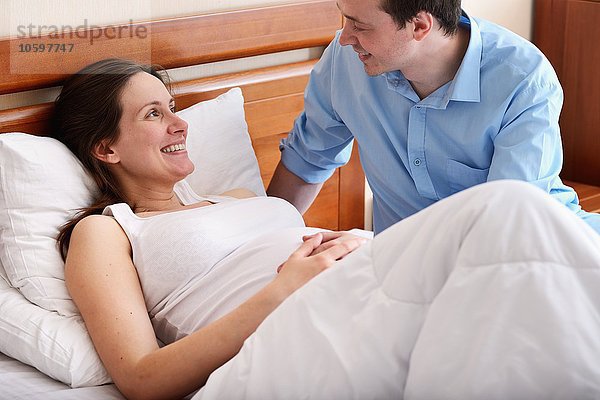 Schwangere Frau im Bett liegend  Mann neben ihr sitzend