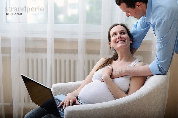 Schwangere Frau im Stuhl sitzend  mit Laptop  Ehemann hält ihre Hand