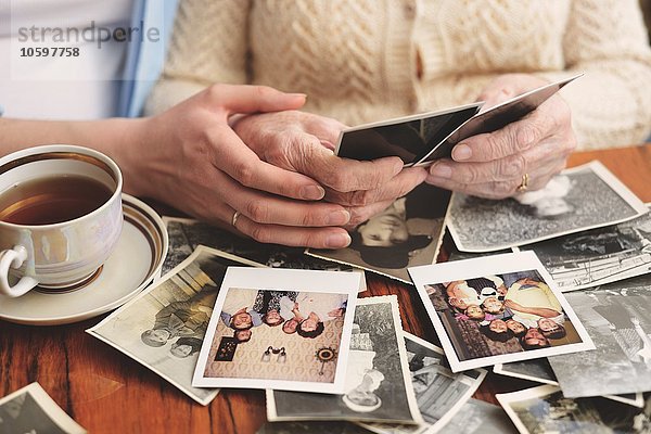 Seniorin und Enkelin am Tisch sitzend  Blick durch alte Fotos  Mittelteil
