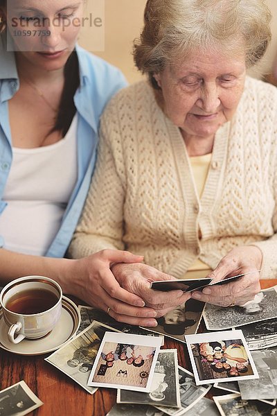 Seniorin und Enkelin sitzen am Tisch und sehen sich alte Fotos an.