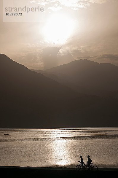 Silhouette von Radfahrern mit Blick auf Berg und See bei Sonnenuntergang  Nepal