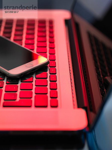 Rotes Licht auf Laptop und Handy illustriert die Gefahr von Hackern