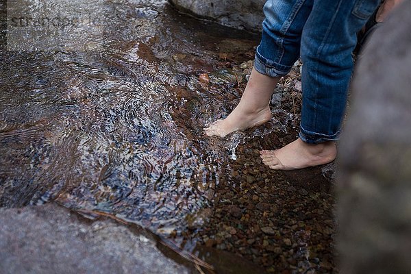 Beine und nackte Füße von Kleinkindern  die über dem Rockpool baumeln.