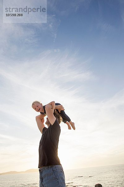 Erwachsener Mann  der seine kleine Tochter am Strand hochhebt  Calvi  Korsika  Frankreich