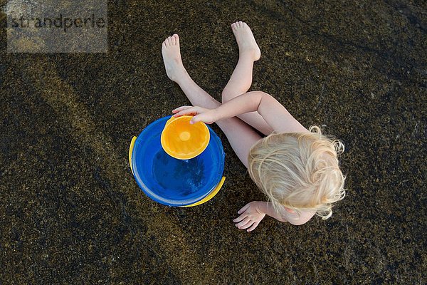 Draufsicht auf das im Sand spielende weibliche Kleinkind mit Spielzeugeimer
