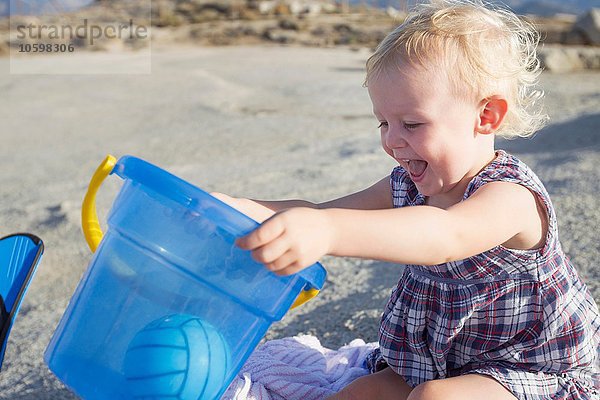 Fröhliches weibliches Kleinkind beim Spielen am Strand mit Spielzeugeimer