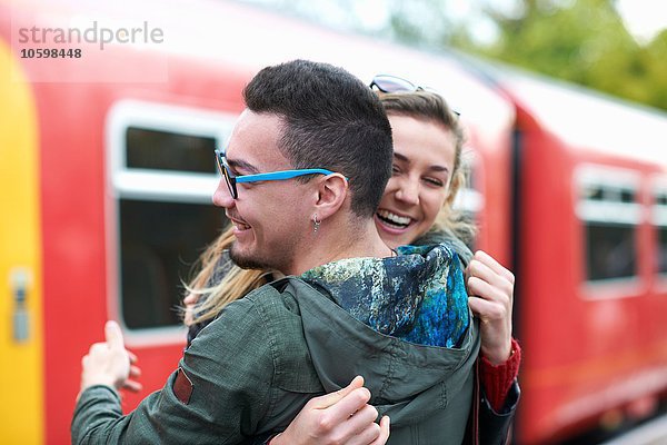 Heterosexuelles Paar  das sich am Bahnhof umarmt  lächelnd