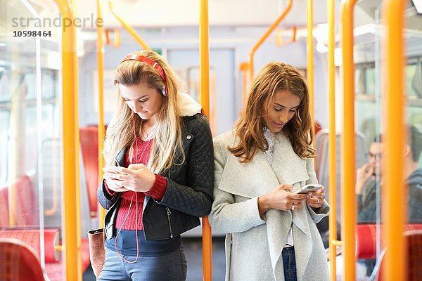 Zwei junge Frauen im Zug  Rücken an Rücken  über Smartphones