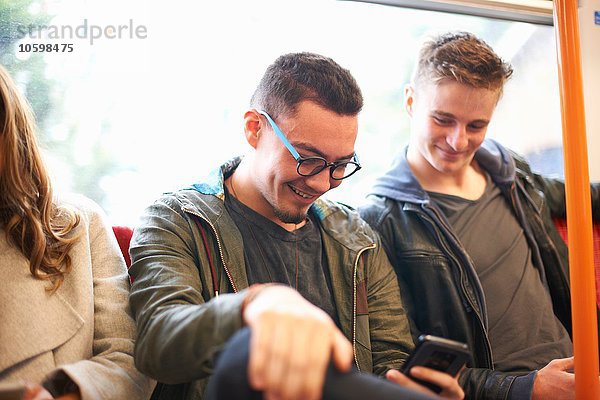 Zwei junge männliche Freunde im Zug  die auf das Smartphone schauen.