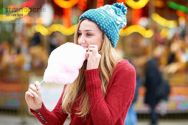 Junge Frau isst Zuckerwatte auf der Kirmes  im Freien