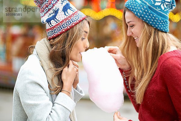 Zwei junge Frauen essen Zuckerwatte auf der Kirmes  im Freien