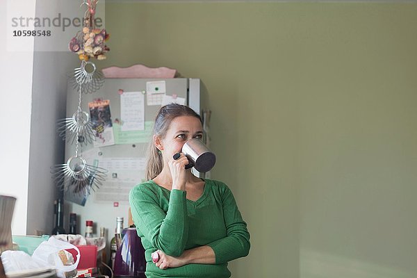 Mittlere erwachsene Frau in der Küche  die aus dem Becher trinkt und wegschaut.