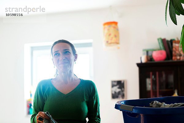 Mittlere erwachsene Frau  die Kleidung im Wäschekorb sortiert und lächelnd wegsieht.