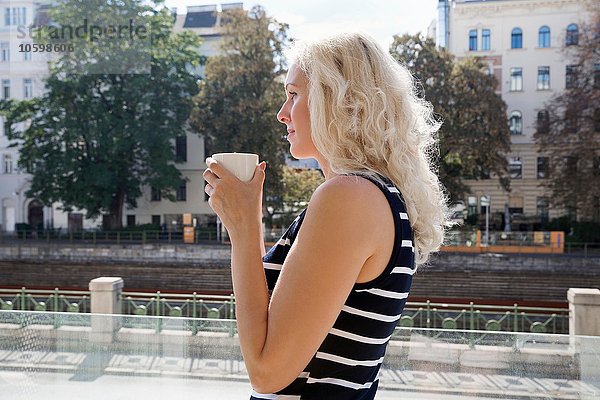 Seitenansicht einer reifen Frau im Freien  die eine Kaffeetasse in der Hand hält.