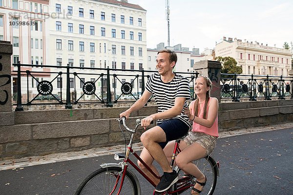 Junger Mann auf dem Fahrrad mit junger Frau auf dem Rücken sitzend lächelnd