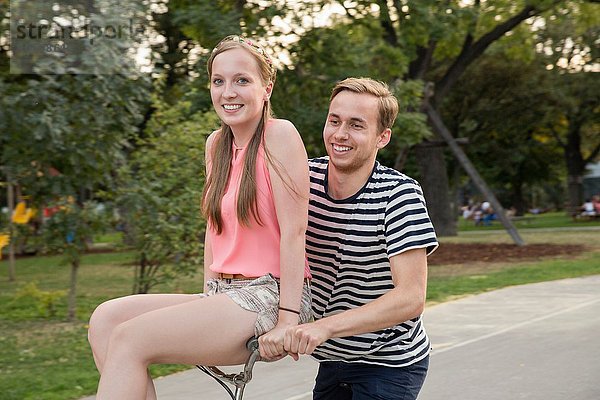 Junger Mann auf dem Fahrrad mit junger Frau am Lenker sitzend lächelnd