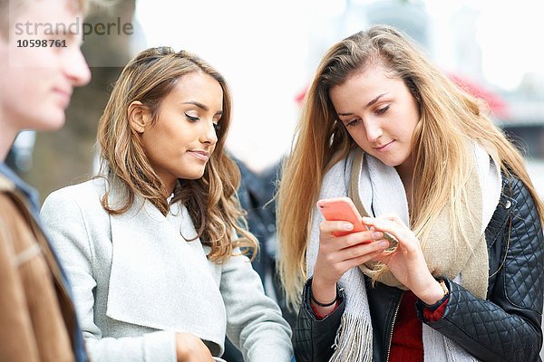 Junge Frau mit Freunden beim Lesen von Smartphone-Texten auf der Straße