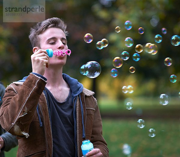 Junger Mann bläst Blasen im Herbstpark