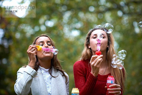 Zwei junge Freundinnen blasen Blasen im Park