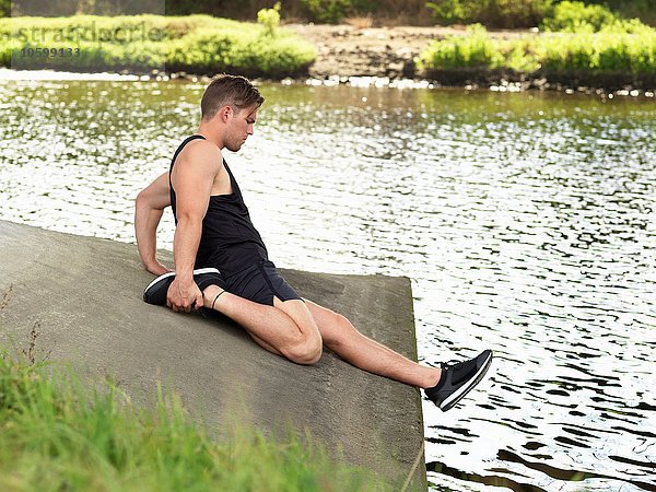 Junger Mann trainiert am Fluss  Bein strecken
