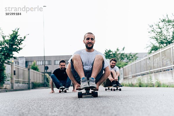 Drei junge Männer sitzen auf Skateboards.