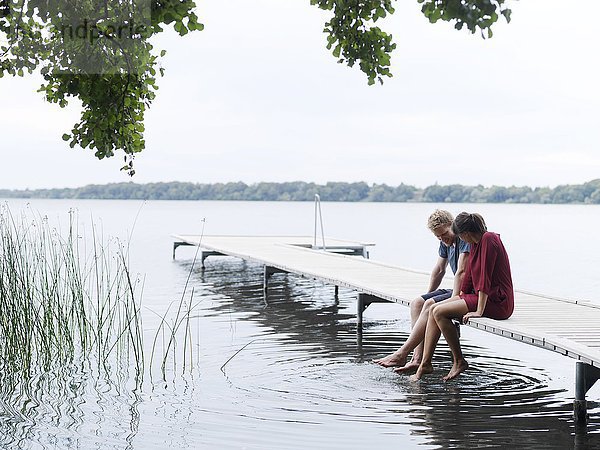 Paar sitzt auf dem Pier nebeneinander und taucht Zehen ins Wasser  Kopenhagen  Dänemark
