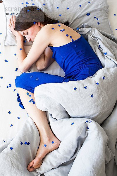 Overhead-Ansicht einer reifen Frau im blauen Pyjama  die in einem sternenbedeckten Bett liegt.