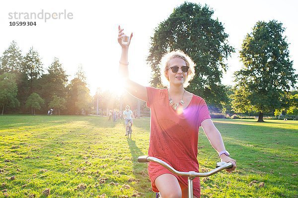 Partygängerin mit Wein  die bei Sonnenuntergang mit dem Fahrrad im Park ankommt.