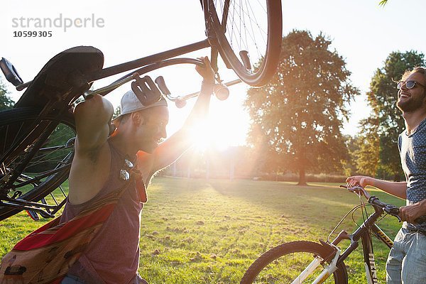 Zwei männliche Freunde  die mit Fahrrädern bei Sonnenuntergang im Park ankommen.