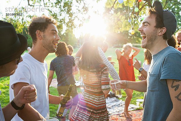 Gruppe erwachsener Freunde beim Plaudern auf der Party im Park bei Sonnenuntergang