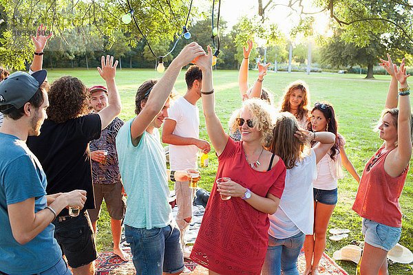 Eine Menge erwachsener Freunde tanzt auf einer Party im Park bei Sonnenuntergang.