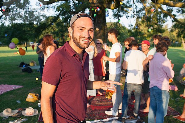 Porträt eines jungen Mannes auf einer überfüllten Party im Park bei Sonnenuntergang