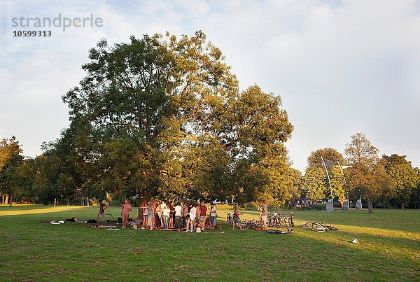 Fernsicht auf erwachsene Menschenmenge unter einem Baum bei Sonnenuntergang im Park