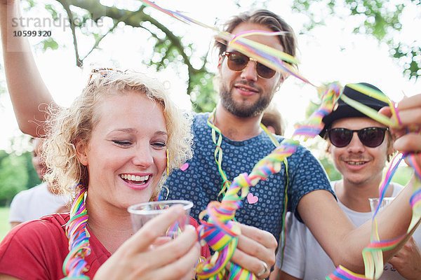 Erwachsene Freunde  die sich bei der Sonnenuntergangsparty im Park in Luftschlangen einwickeln.