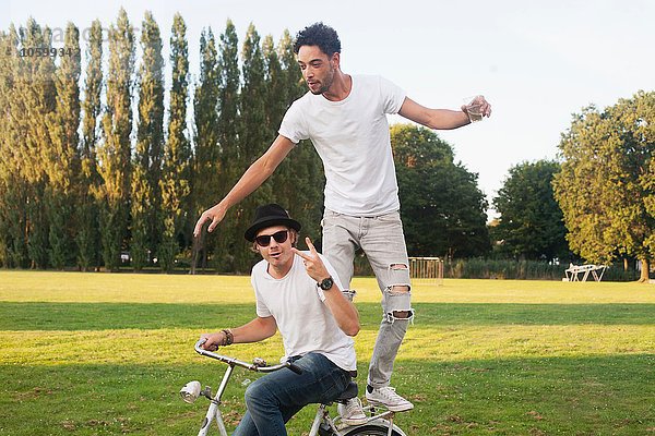 Zwei männliche Freunde  die mit dem Fahrrad im Park herumtollen.