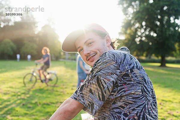 Porträt eines jungen Mannes  der im sonnigen Park über die Schulter schaut.