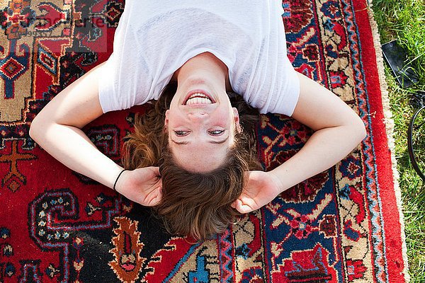 Draufsicht auf eine junge Frau  die auf einem Teppich liegt.
