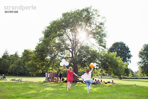 Rückansicht von zwei jungen Frauen  die mit Luftballons auf der Parkparty tanzen.