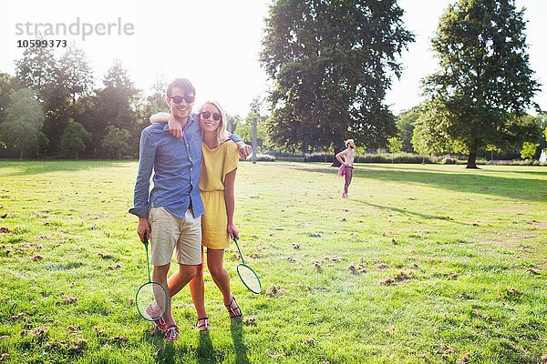 Romantisches junges Paar mit Badmintonschlägern im sonnigen Park