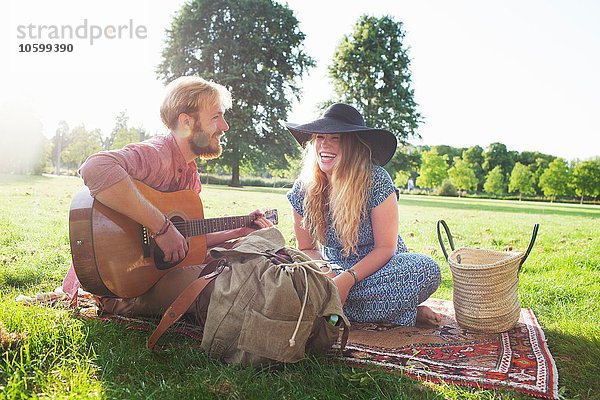 Romantisches junges Paar spielt Akustikgitarre im Park