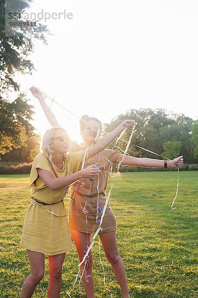 Zwei junge Frauenfreunde  die sich auf der Party im Park in Luftschlangen wickeln