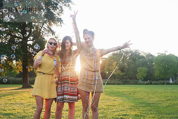 Porträt von drei jungen Frauen  die sich auf einer Party im Park in Luftschlangen wickeln.